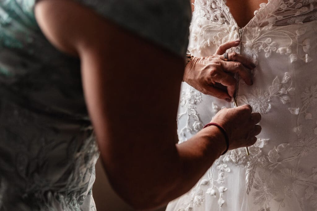 Bride’s Mom Buttoning Dress (Close-Up) Title: Mother of the Bride Helping with Dress at Pittsburgh Airport Marriott Alt: Close up of mother of the bride buttoning wedding dress in hotel room at Pittsburgh Airport Marriott