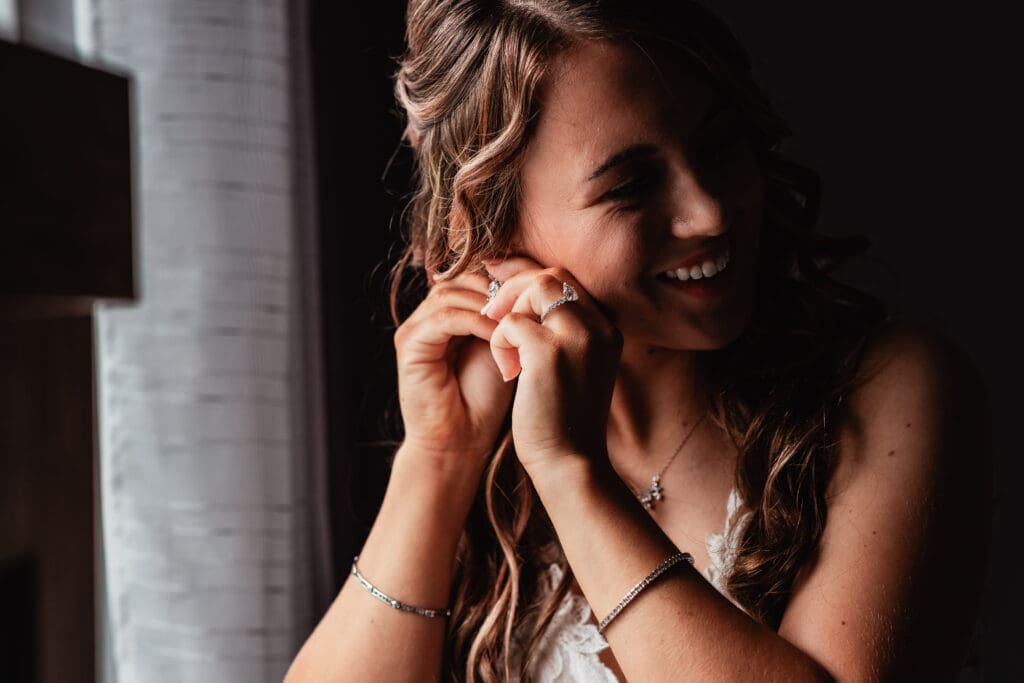 Bride in lace dress stands by window in soft light at Hinckston Run Farm