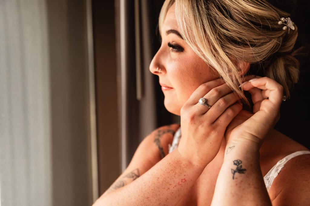 Pittsburgh bride looking out window while she puts in her earrings at Pittsburgh Airport Marriott