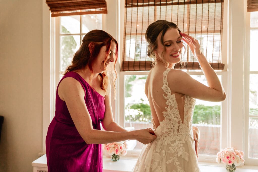 Pittsburgh bride being helped into her wedding dress by her mother in front of a bay window at Phipps Botanical Gardens
