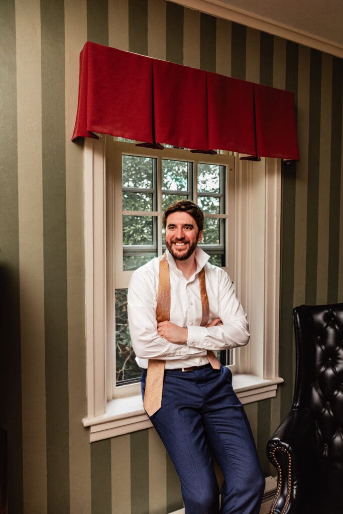 Groom leaning against window and posing for wedding portraits at Succop Nature Park