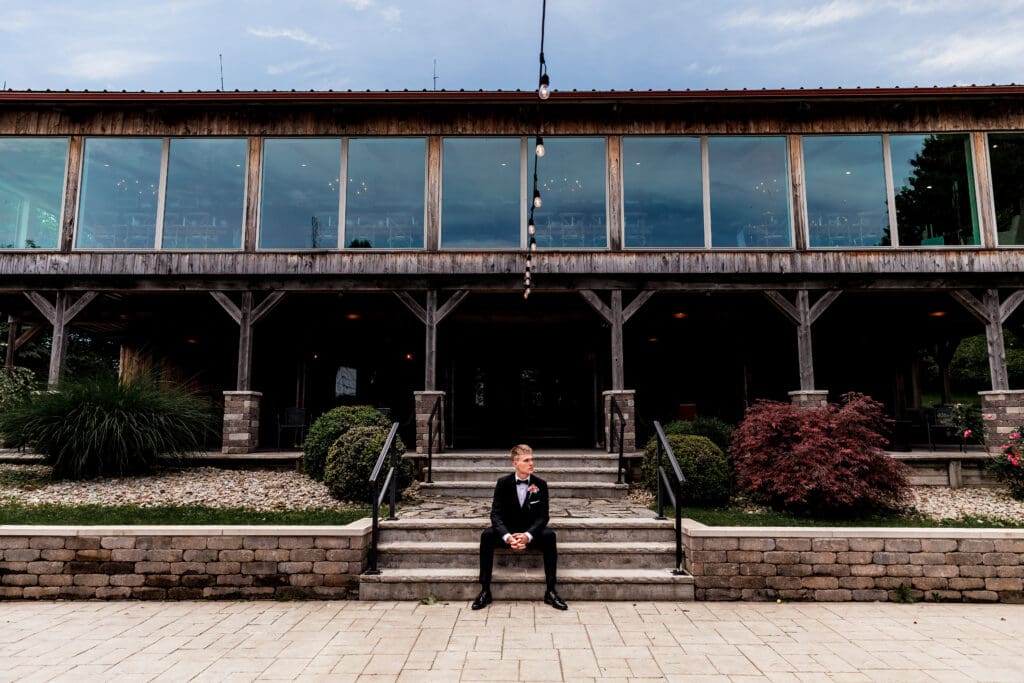 Groom sits on stairs at the Willowbrook wedding venue