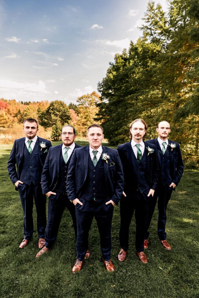 Groom and groomsmen forming Flying V in front of fall foliage and pond at Pinehall at Eisler Farm