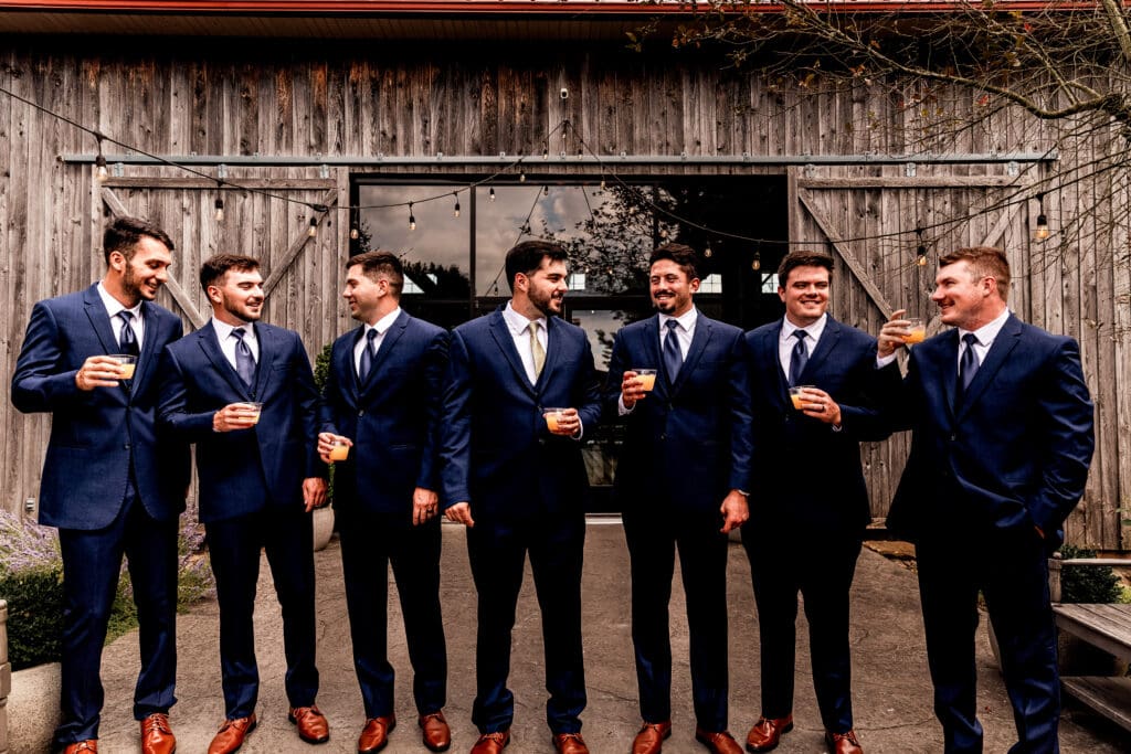Groom and groomsmen clinking drinks together outside the Willowbrook event barn in Volant, PA