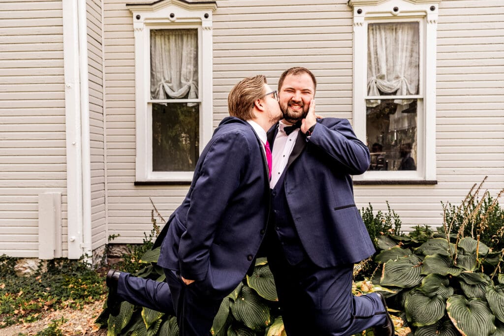 Groomsman kissing the groom on the cheek during portraits at The Gathering Place at Darlington Lake