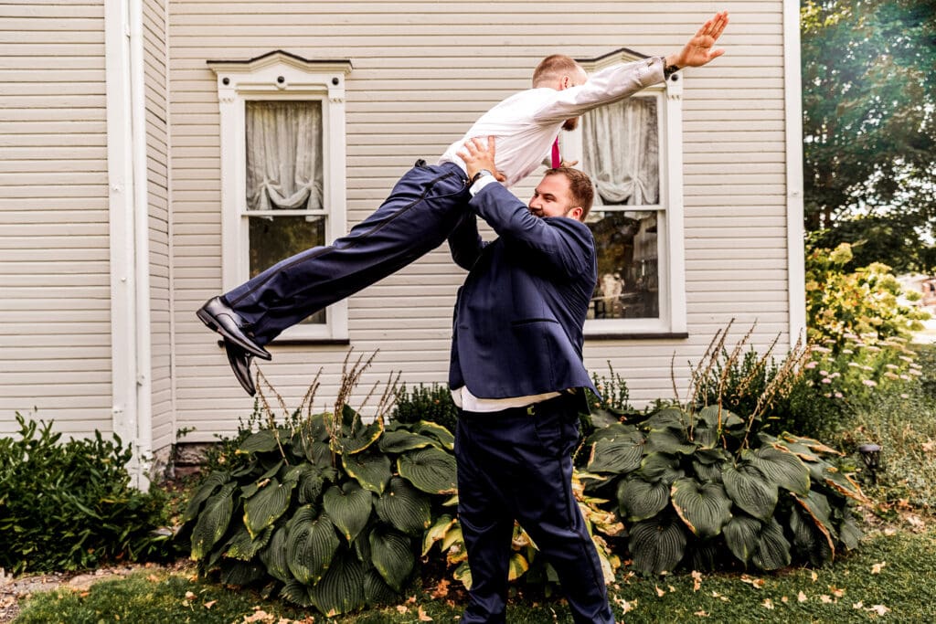 Groom lifting a groomsman into the air during portraits at The Gathering Place at Darlington Lake