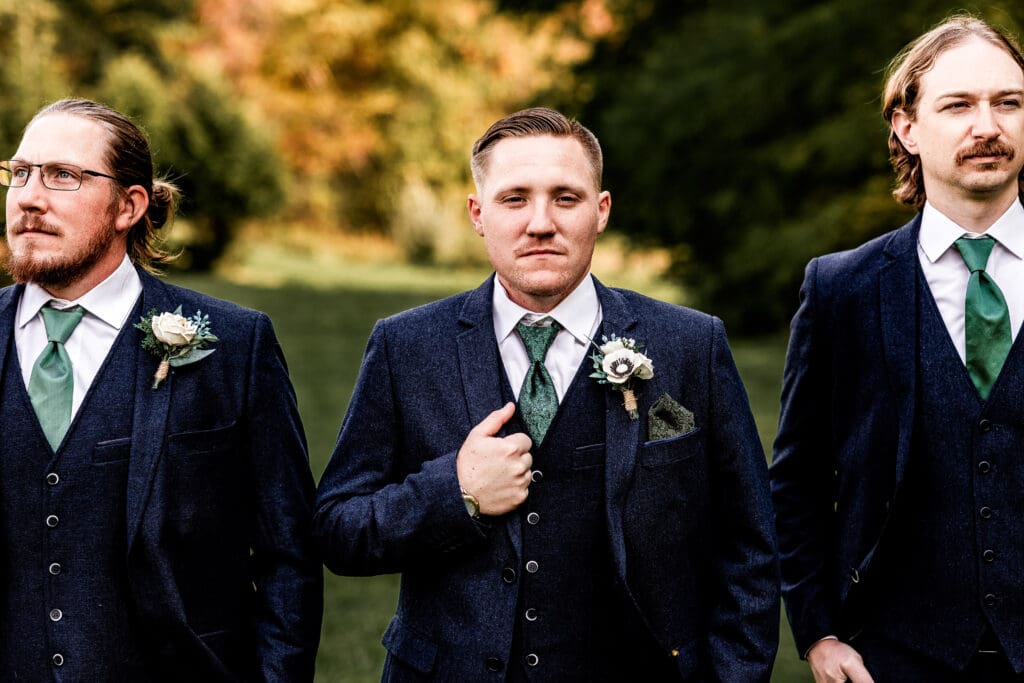 Close-up of groom and groomsmen in front of fall foliage and pond at Pinehall at Eisler Farm