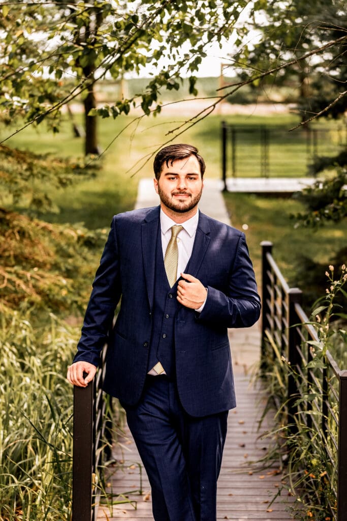 Pittsburgh groom holding his lapel and looking confidently at the camera during Willowbrook wedding portraits in Volant, Pennsylvania