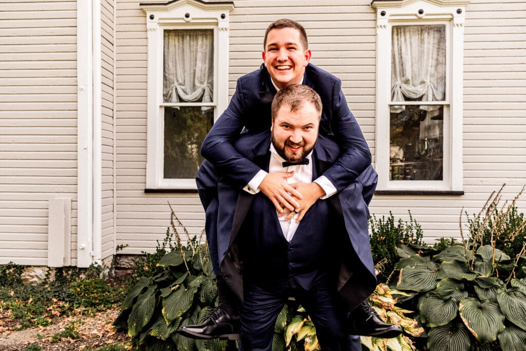 Groom carrying a groomsman piggyback style during portraits at The Gathering Place at Darlington Lake