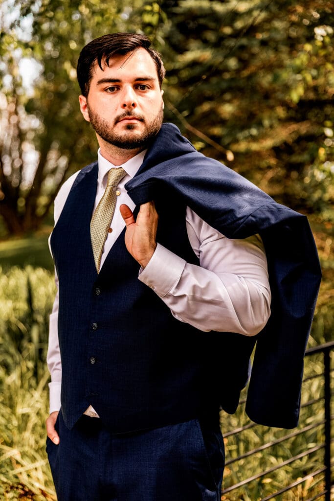 Groom slings jacket over his shoulder during portraits at Willowbrook wedding in Volant, PA