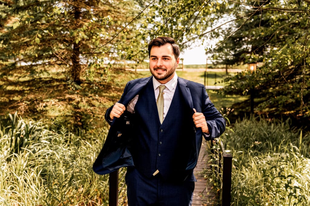 Pittsburgh groom smiling while adjusting his jacket during Willowbrook wedding portraits in Volant, Pennsylvania