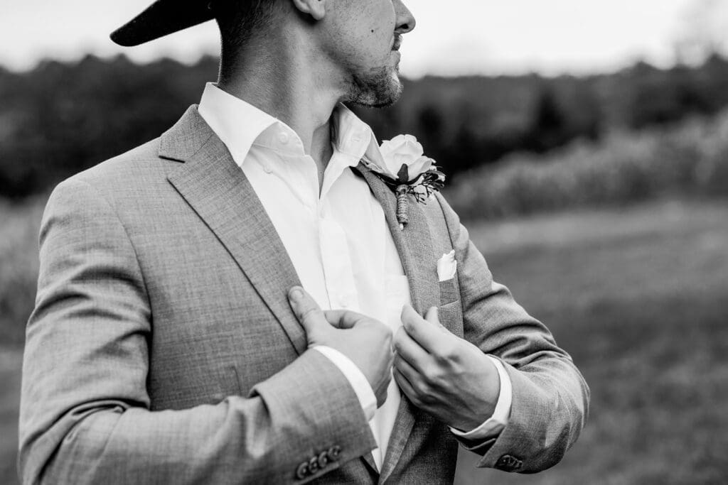 Black and white photo of groom adjusting boutonniere at Hinckston Run Farm wedding