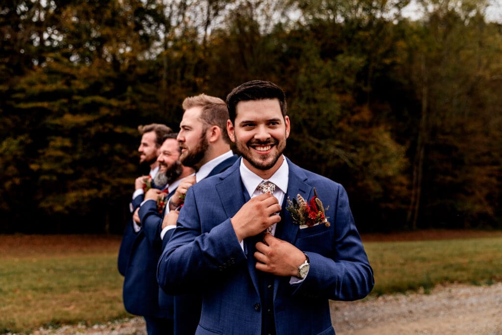 Groom looks at camera as groomsmen fix ties behind him at Hinckston Run Farm