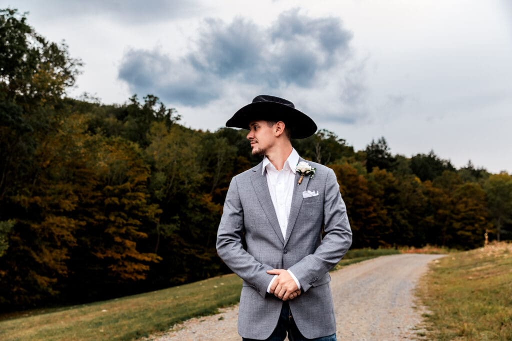 Groom in gray blazer standing on rural hilltop path under cloudy skies at Hinckston Run Farm