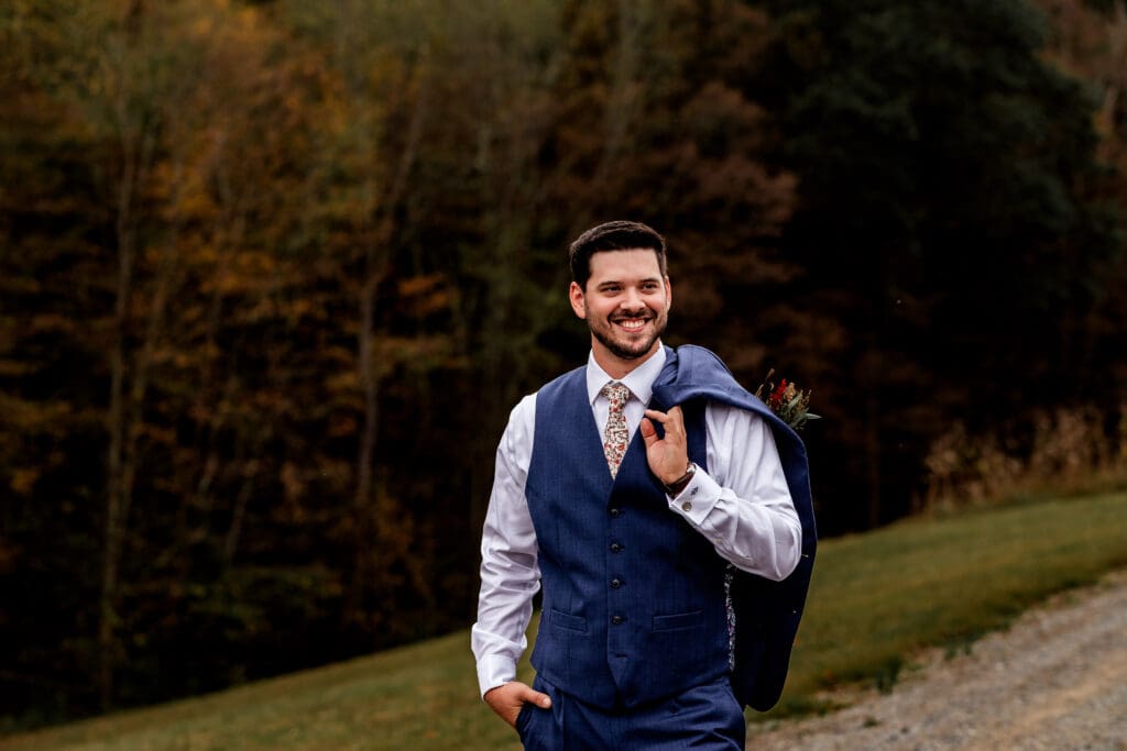 Groom stands on wooden path with jacket over shoulder at Hinckston Run Farm