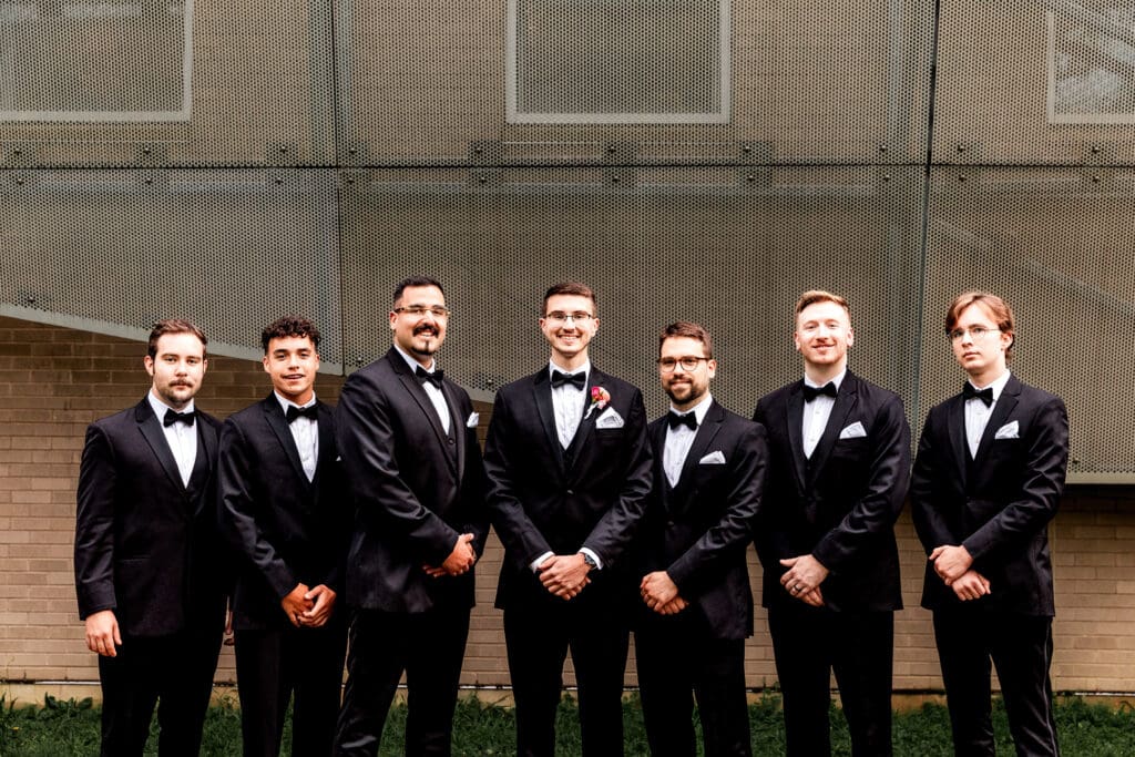 Groom and groomsmen in black suits posing in front of the National Aviary