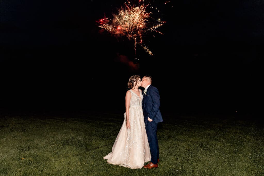 Wedding couple sharing a kiss as fireworks light up the sky at Pinehall at Eisler Farm wedding reception