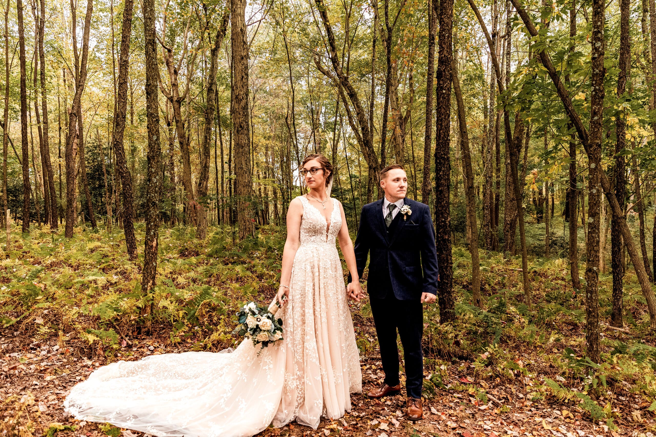 Bride and groom holding hands and looking in opposite directions in fern field at Pinehall at Eisler Farm