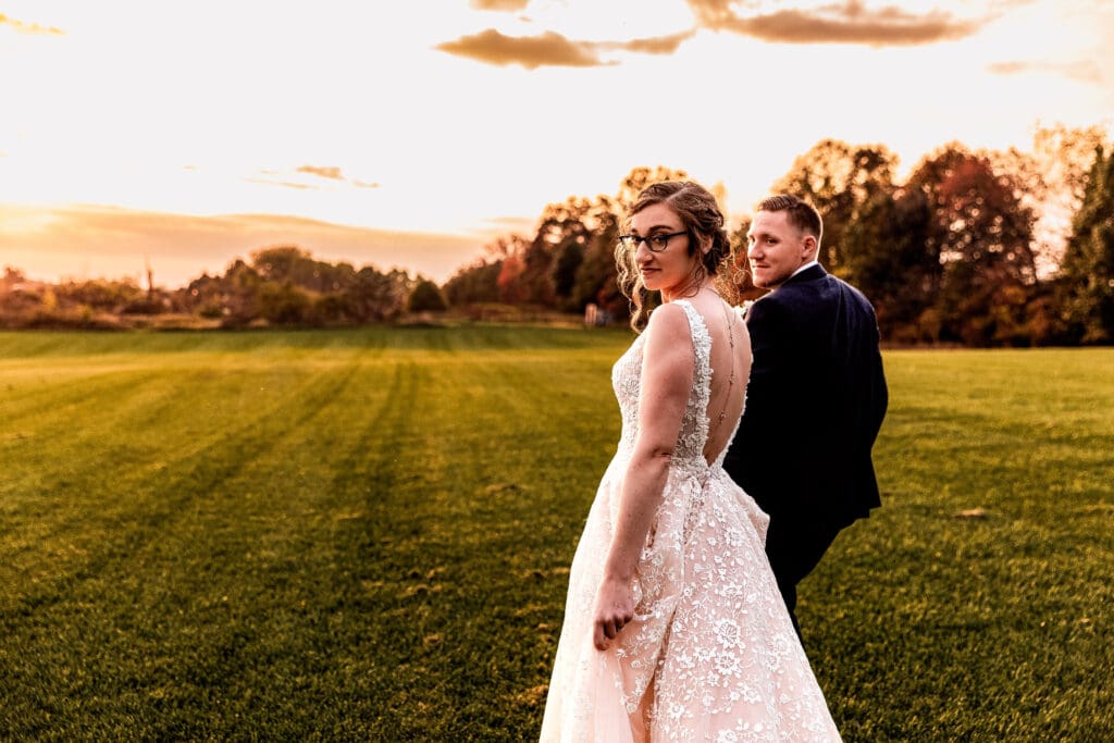Pittsburgh bride glances back at camera as groom leads her into sunset at Pinehall at Eisler Farm