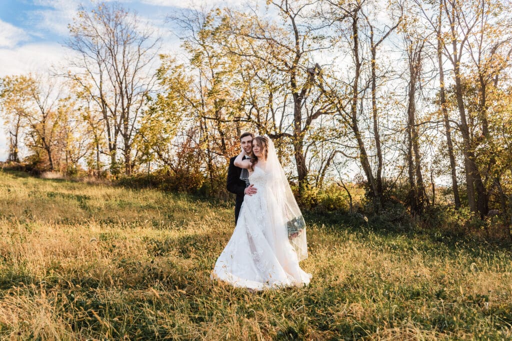 Wedding couple embraces in an open field at sunset during their Cozzi Acres ceremony