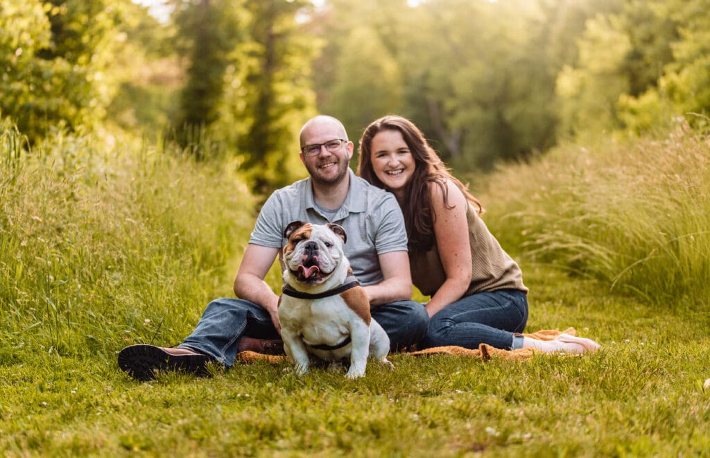 Couple sits together and poses with their bulldog during a relaxed engagement photo session outdoors