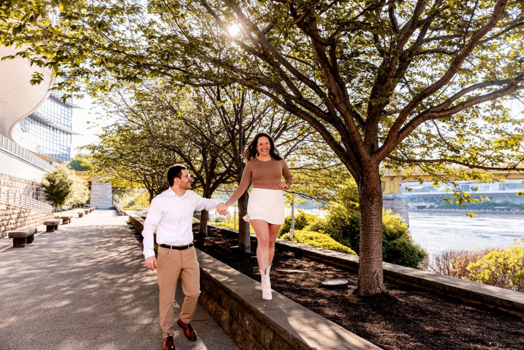 Scenic tree-lined waterfront pathway in Pittsburgh with people walking and enjoying a sunny day during an engagement session