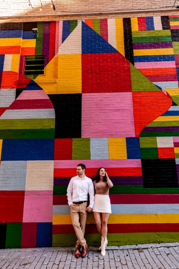 Couple stands in front of a colorful geometric mural with bold red, yellow, blue, and pink stripes during a Pittsburgh engagement session