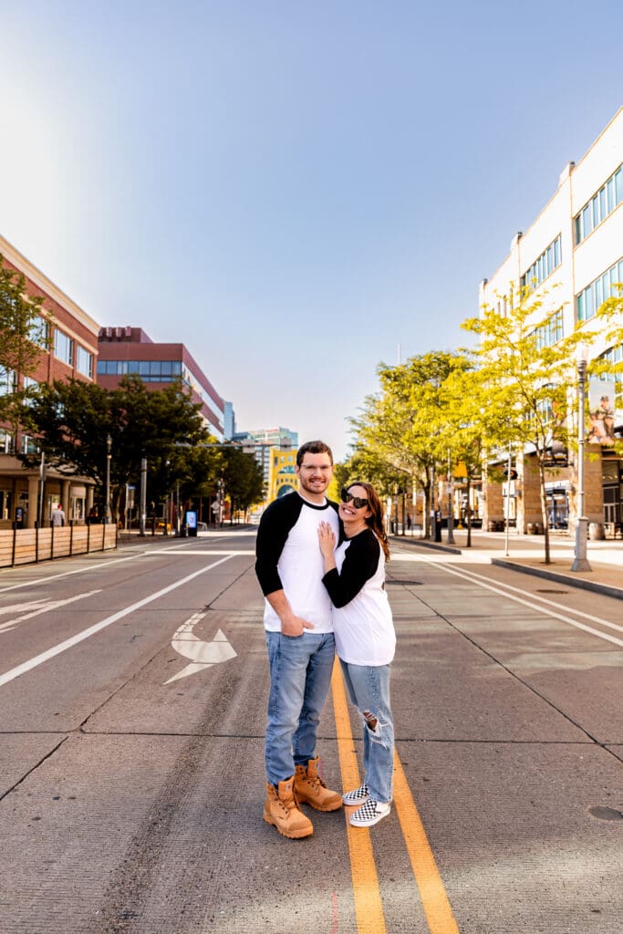 Couple poses playfully on an empty Pittsburgh urban street with yellow trees and modern buildings in the background