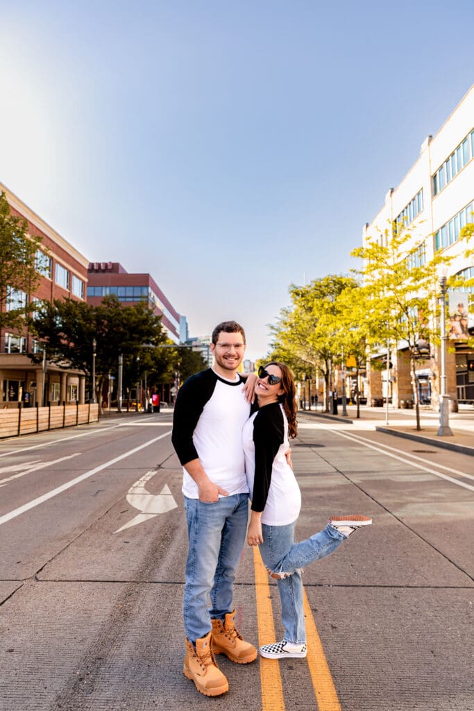 Couple stands together on an empty urban street in Pittsburgh lined with buildings and trees on a sunny day