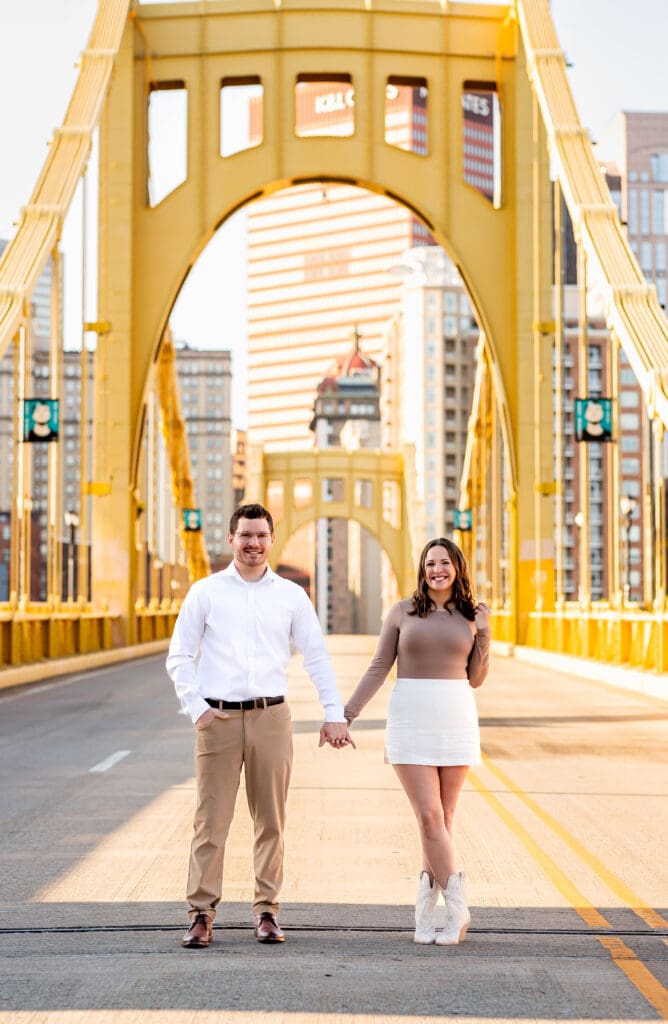 Couple stands together on the yellow Roberto Clemente Bridge in Pittsburgh during a romantic engagement photo session
