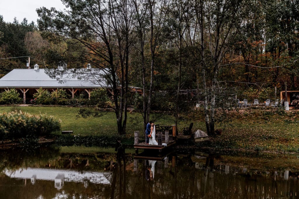 Couple embraces on dock with reception barn behind them at Hinckston Run Farm