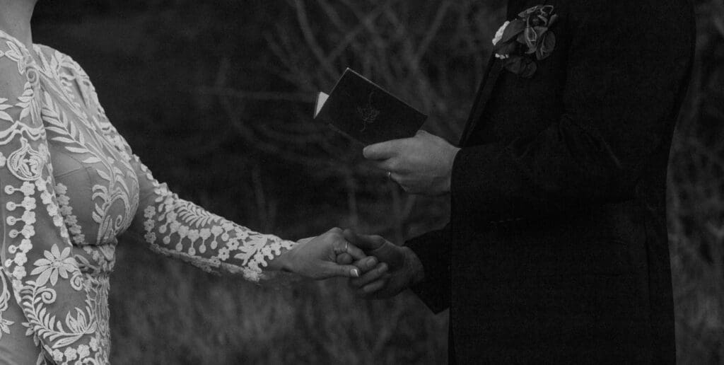 Black and white close-up of a couple holding hands during their Moab elopement vows, capturing intimate desert wedding moments and emotional connection.