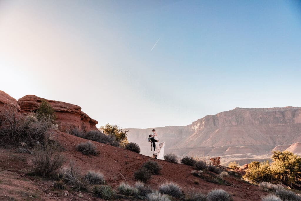 Groom lifting his bride in a joyful moment after their adventurous elopement in the desert landscape near Moab, Utah.