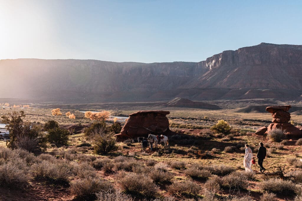 Couple walking back to their horses at a Moab elopement during sunset, with dramatic desert mesas and warm golden light in the background.