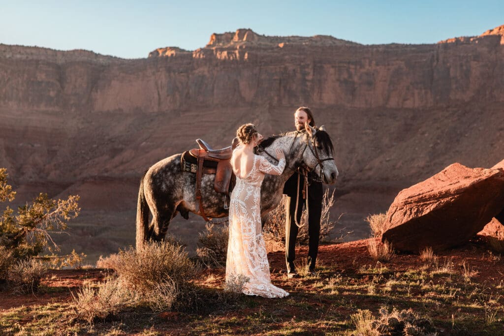 Couple petting a horse after their Moab elopement sunset ceremony, surrounded by red rock cliffs and golden desert light.