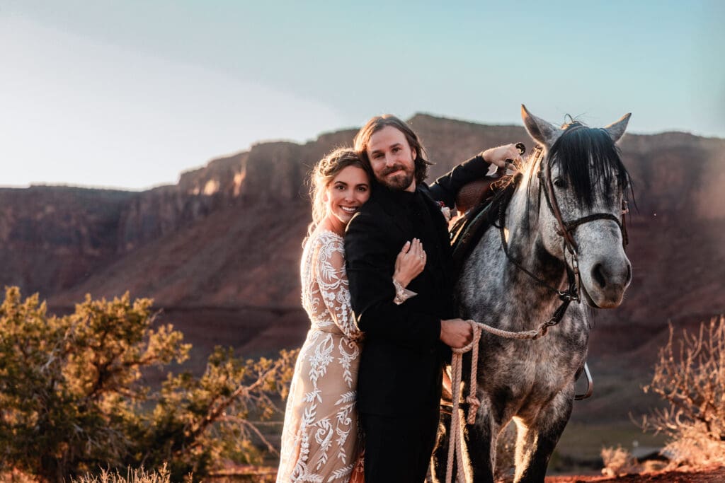 Bride hugging her groom from behind at golden hour during their Moab wedding, both smiling with red rock mesas glowing in the sunset light.