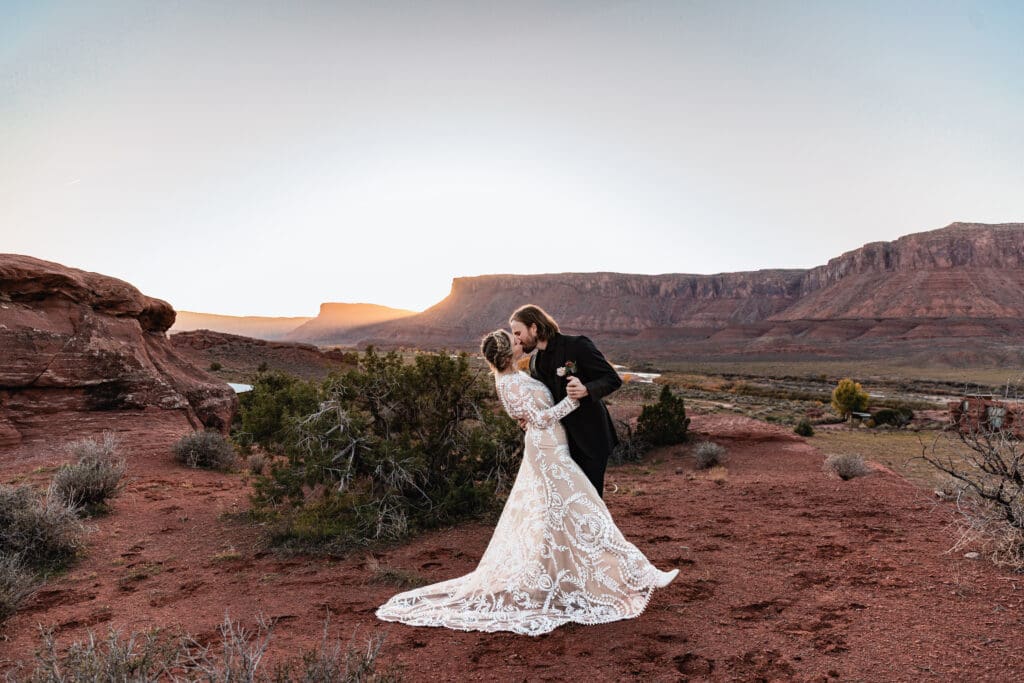Couple sharing a romantic dip kiss at sunset during a Moab elopement, with red rock mesas in the background and warm golden light over the desert landscape.
