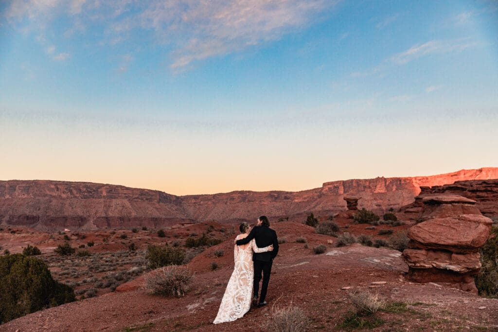 Newlywed couple walking arm in arm into the sunset after their Moab elopement, with red rock desert scenery and warm golden light creating a romantic desert backdrop.