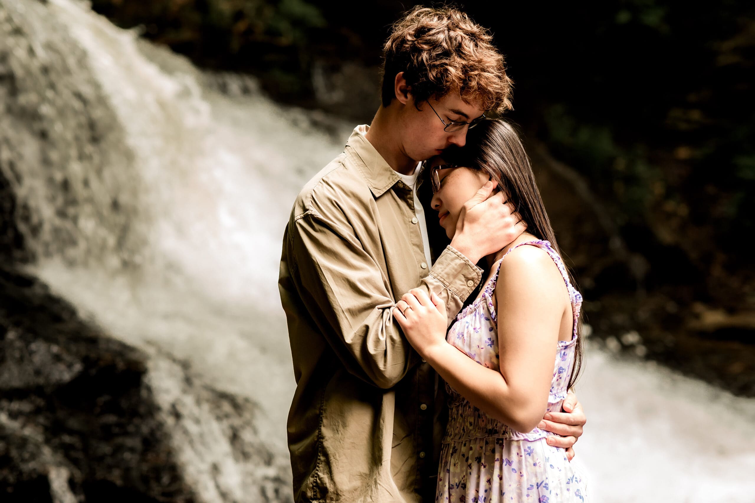 Romantic couple embraces near a cascading waterfall at McConnells Mill State Park during a formal forest engagement photo session