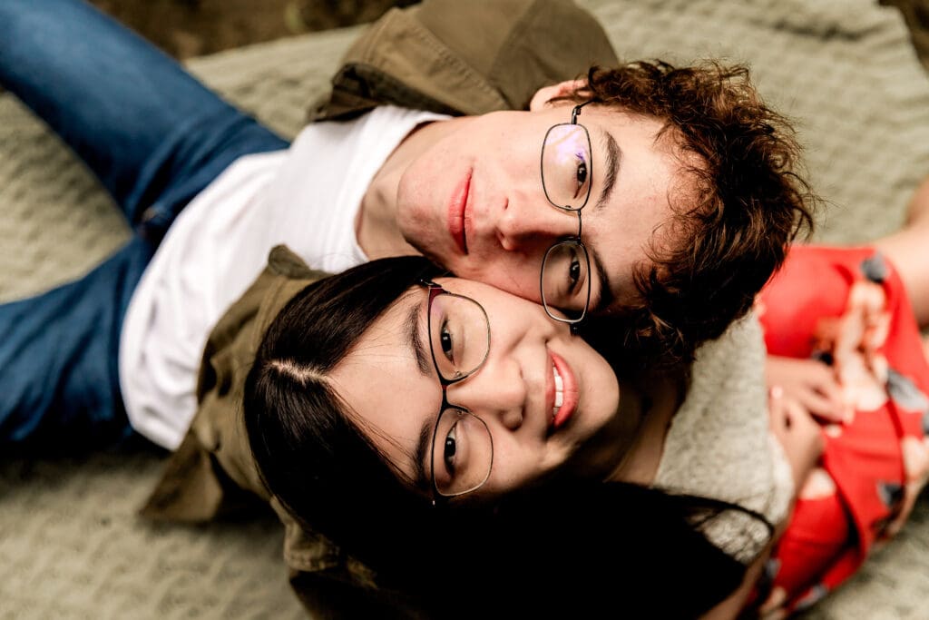 Couple sits back to back and looks up at the camera during a playful engagement portrait session at McConnells Mill State Park