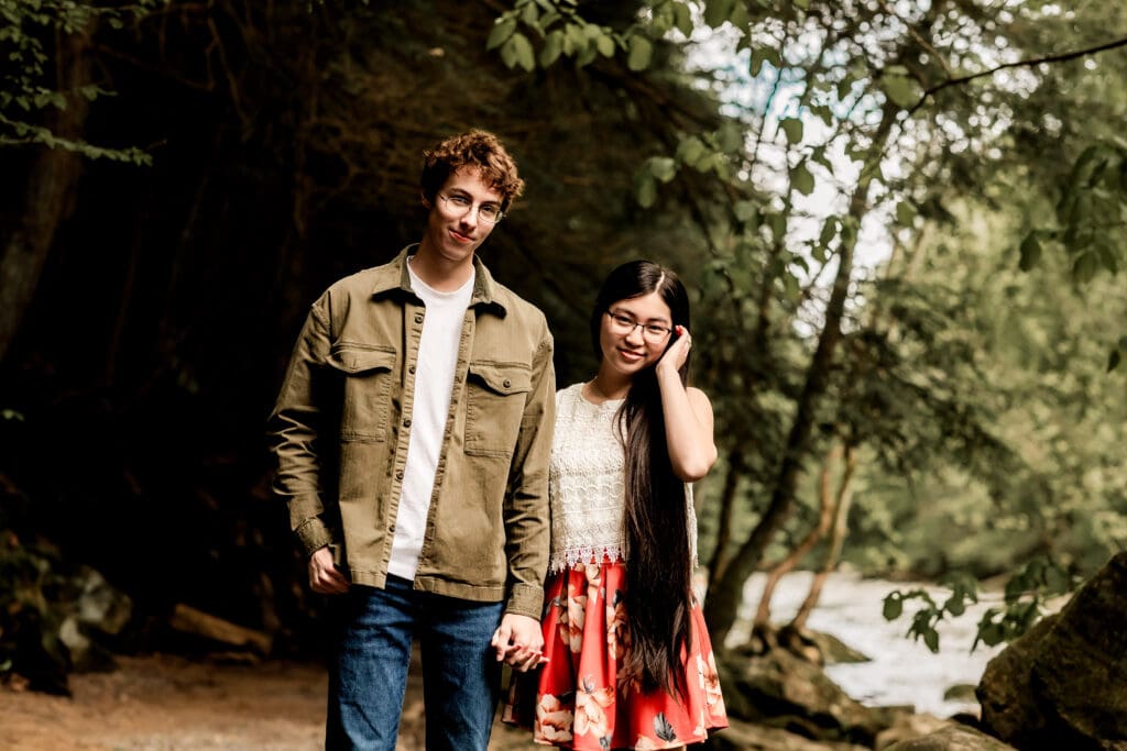 Couple walks together on a wooded path during a romantic outdoor engagement session at McConnells Mill State Park