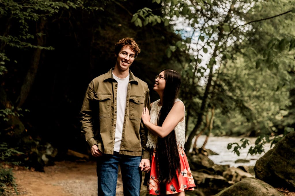Couple walks hand in hand through a scenic wooded path during an spring engagement session at McConnells Mill State Park