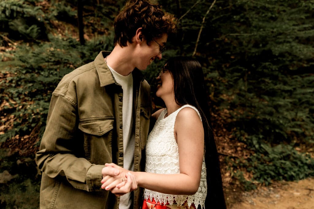 Couple shares a joyful moment together in the woods at McConnells Mill State Park wearing a tan jacket and white lace dress