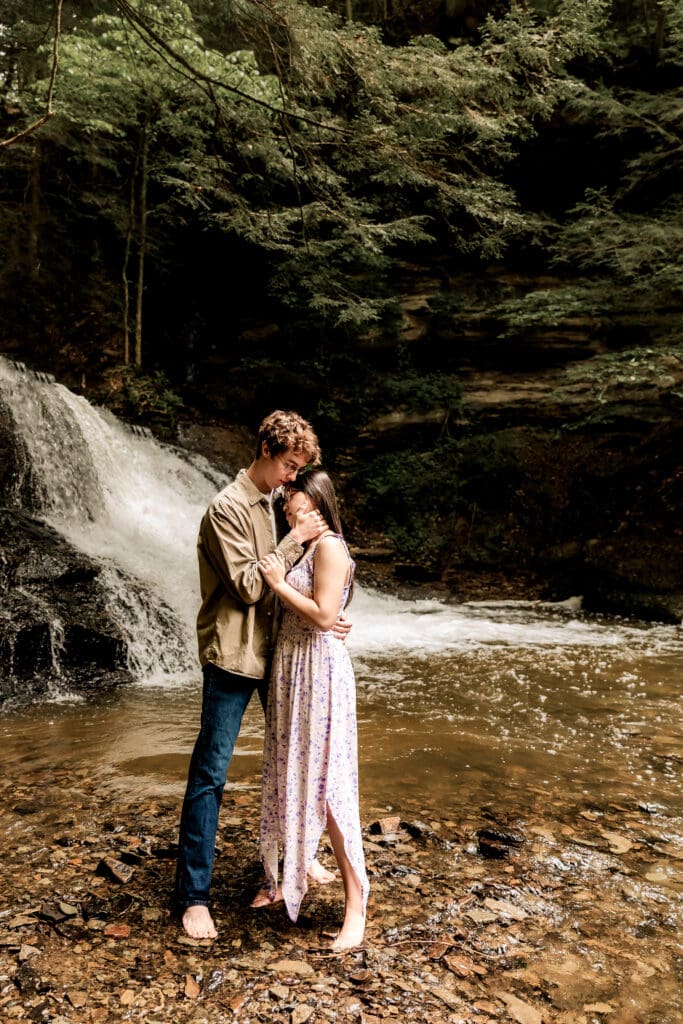 Couple shares a romantic moment near a cascading waterfall surrounded by lush forest at McConnells Mill State Park