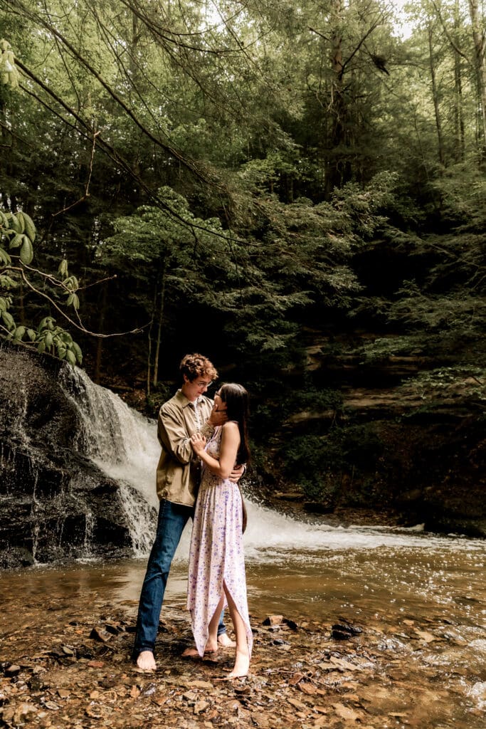 Romantic couple embraces by a waterfall in a lush forest at McConnells Mill State Park, creating an intimate moment in nature