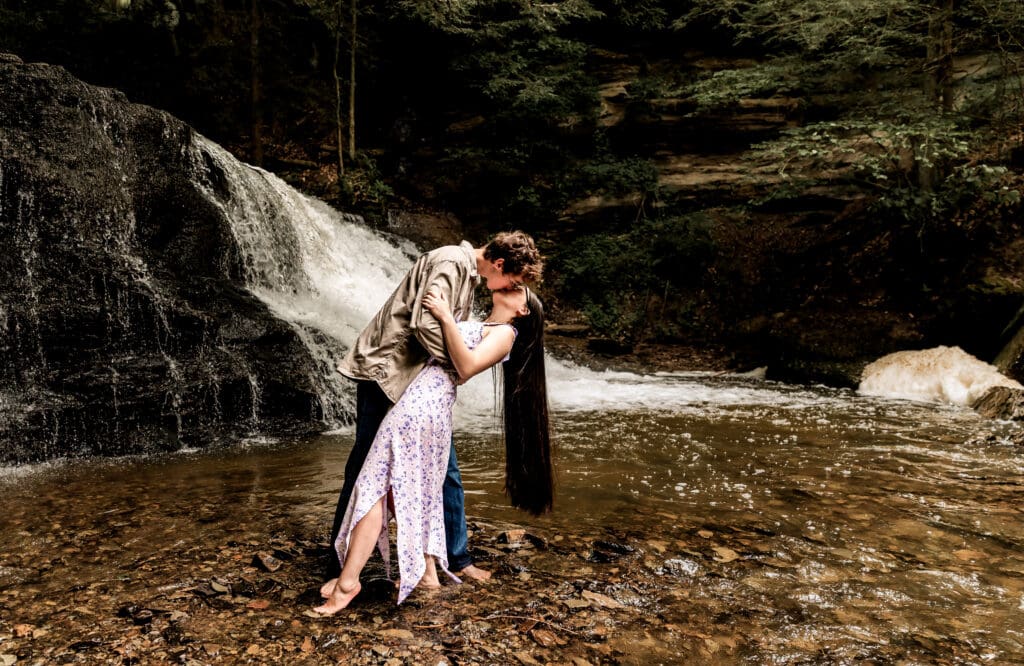 Romantic couple shares an intimate kiss outdoors during a tender engagement photo series at McConnells Mill State Park
