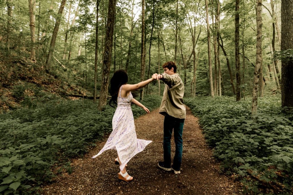 Two people dance together holding hands on a forest path surrounded by lush green foliage at McConnells Mill State Park
