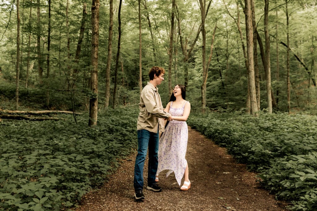 Two people hold hands while walking along a forest trail surrounded by lush green foliage at McConnells Mill State Park