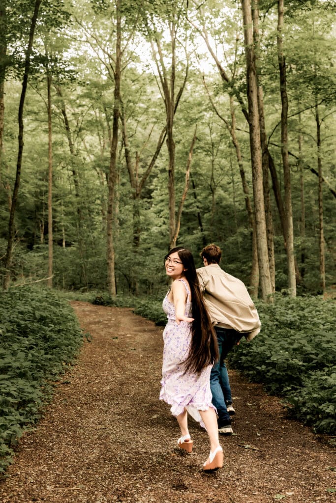 Couple walks hand in hand through a scenic wooded path during an spring engagement session at McConnells Mill State Park