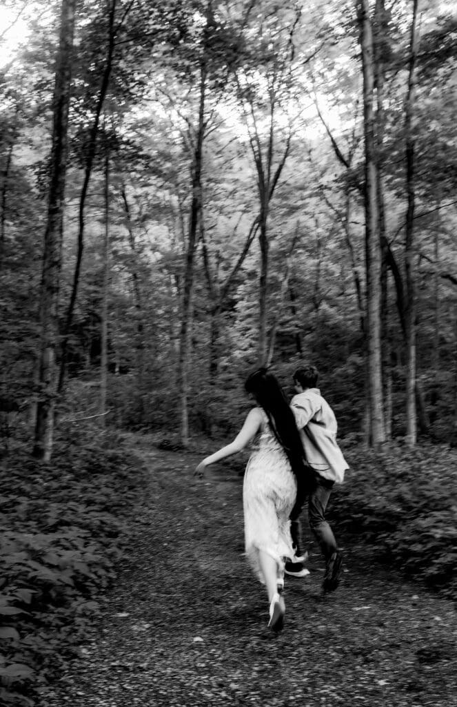 Black and white photograph of two people running playfully down a wooded forest path at McConnells Mill State Park